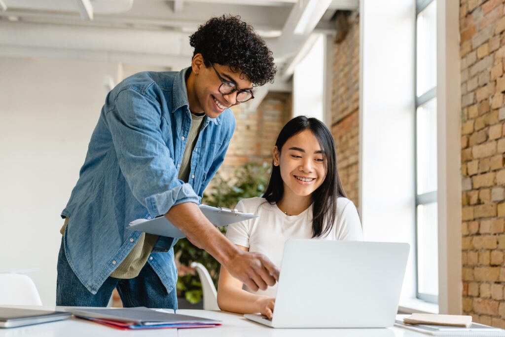Two happy young sales intern sitting with a laptop.